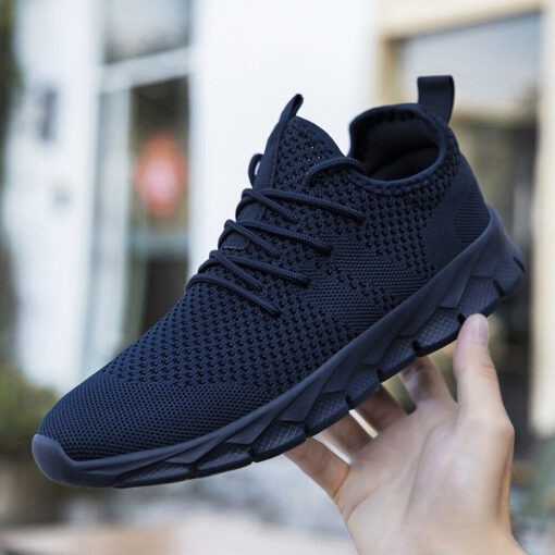 Hand holding black athletic sneaker outdoors.