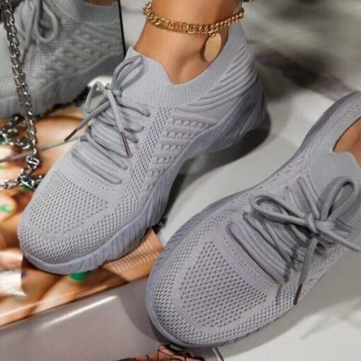 Gray sneakers with ankle bracelet on reflective surface.