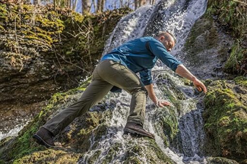 Man climbing mossy rocks by waterfall outdoors